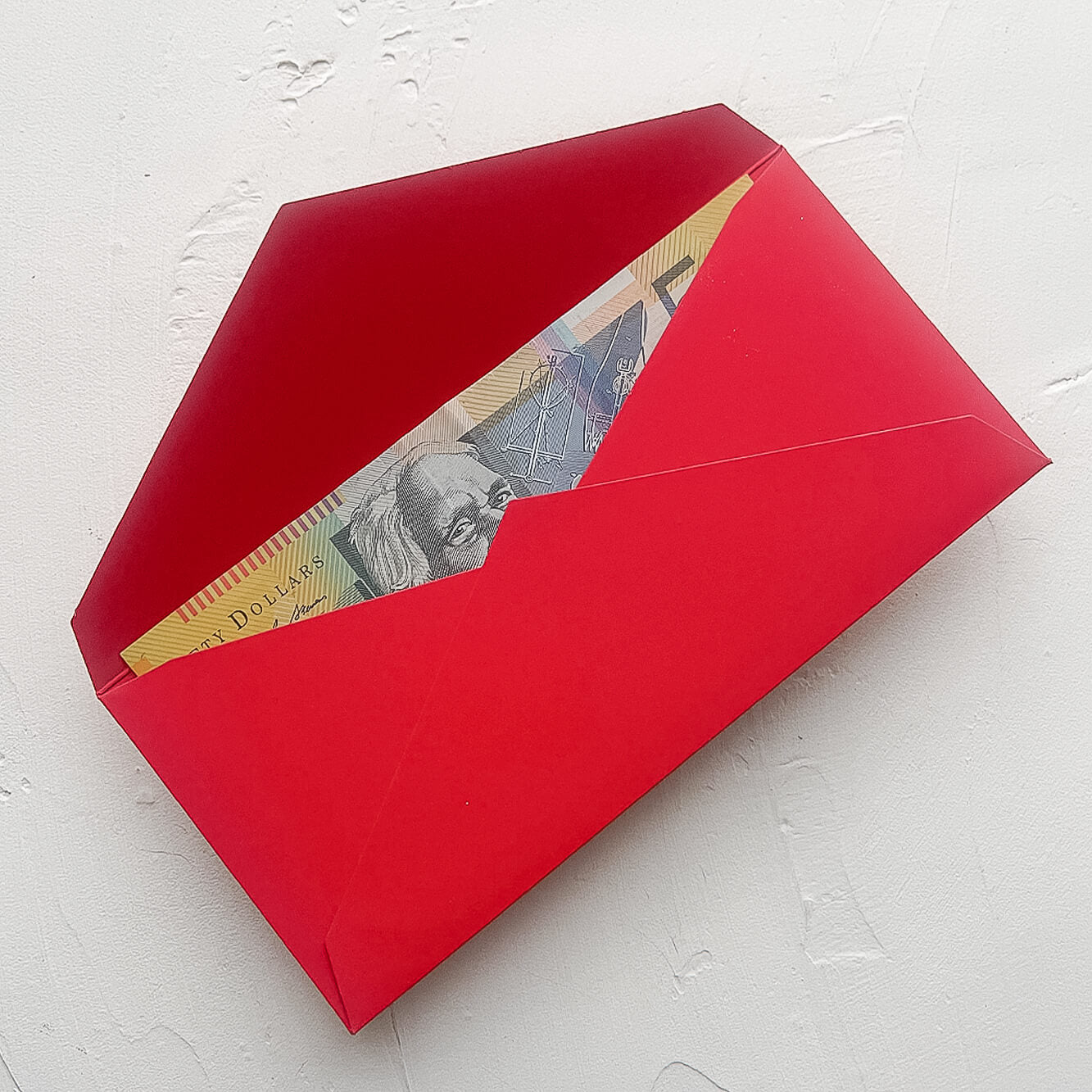 A photo of a red envelope or hongbao or ang pao or lucky packet that is open, showing an Australian fifty dollar note tucked inside..