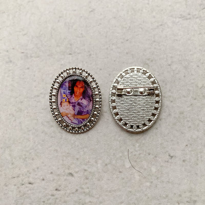 A memorial brooch or memorial pin in the design called Brogue, showing a photo of a young father holding his child, next to the pin back of the memorial brooch, and is intended to be pinned to a wedding bouquet or wedding jacket to include a deceased relative on your wedding day.