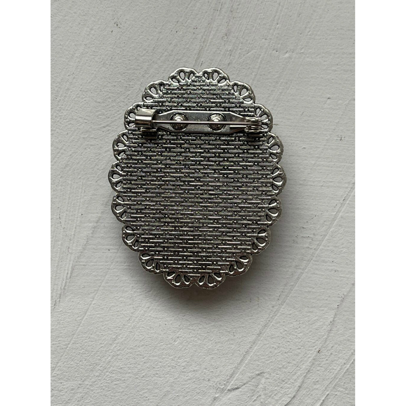 An oval memorial pin or brooch that is no longer manufactured or available to purchase. This memorial pin shows an old woman in black and white and was made to be pinned on to a wedding bouquet or wedding jacket to honour a deceased loved one on your wedding day.