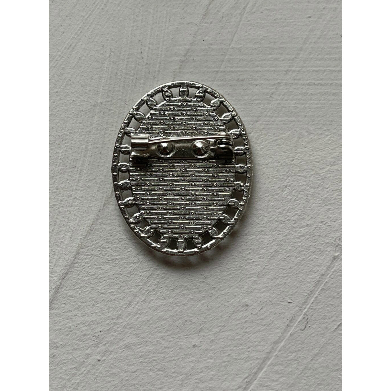 A memorial brooch or memorial pin in the design called Brogue, showing the back of the brooch. The pin back is shown against a neutral white textured background and is intended to be pinned to a wedding bouquet or wedding jacket to include a deceased relative on your wedding day.
