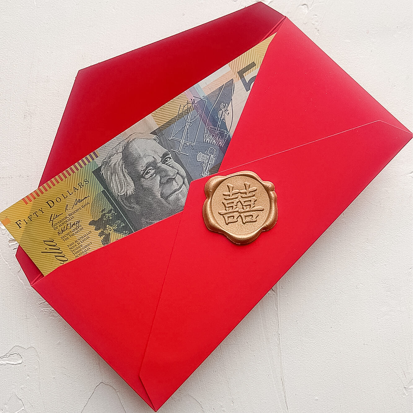 A photo of a red envelope or hongbao or ang pao or lucky packet that is open, showing an Australian fifty dollar note and a premade self adhesive gold wax seal that shows the Chinese calligraphy for double happiness.
