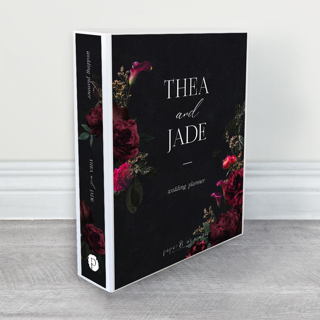 A wedding planner, guide and organiser in a moody floral design with magenta, burgundy and pink flowers and dark emerald green leaves on a black background