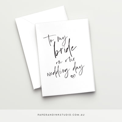 A white folded wedding card in a design called Thorne with black writing that says to my bride on our wedding day with a love heart below it, for the groom or other bride to give to them on their wedding day.